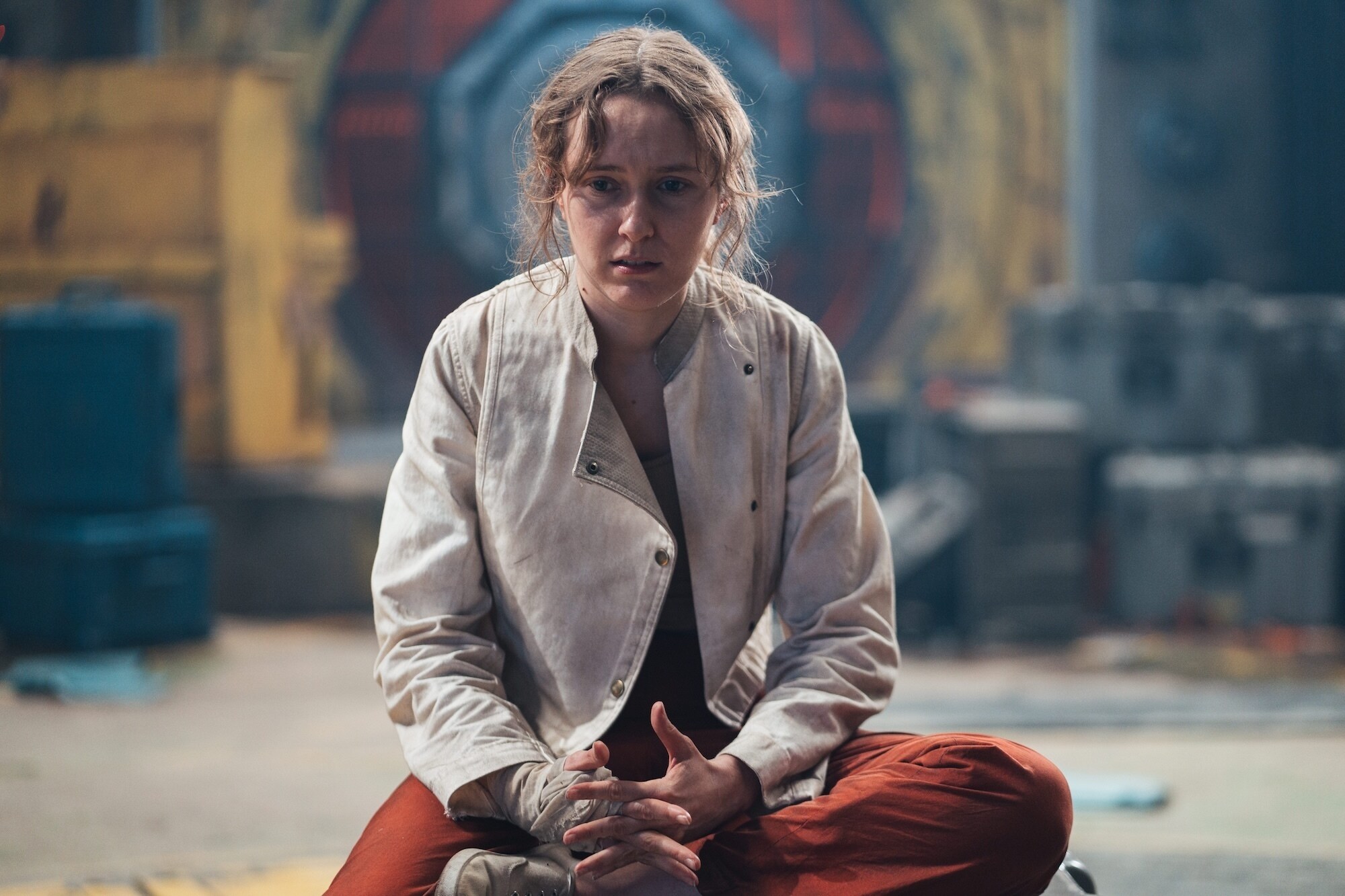 Rose Ayling-Ellis as Aliss sitting on a box scared.